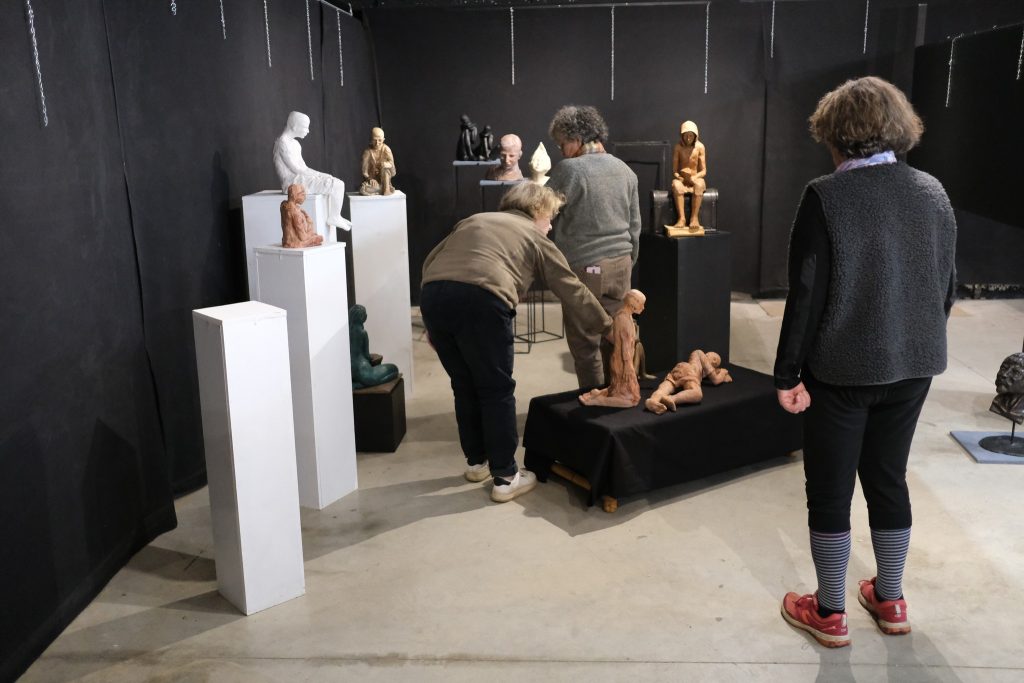 Artistes de dos qui installent leurs sculptures sur des plots dans la galerie associative du TEC