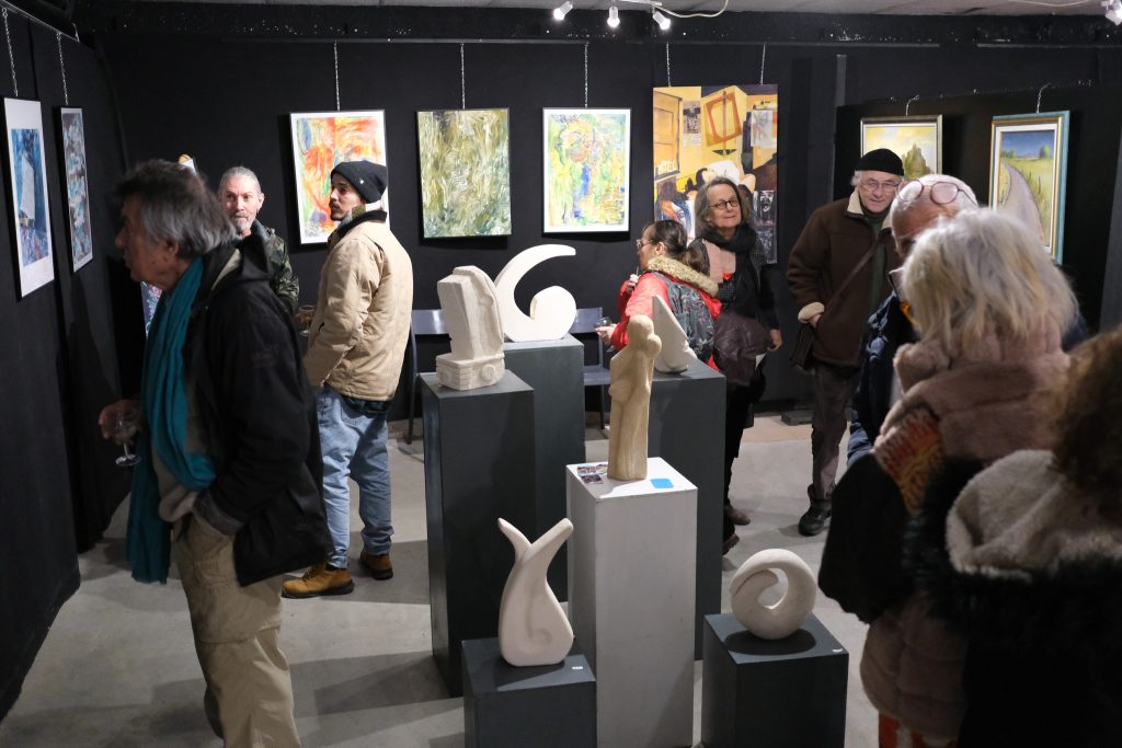 Public du tec en train de regarder des toiles peintes accrochées au mur et des sculptures en pierre sur des socles