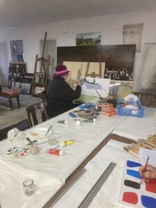 Un homme de dos peint devant un chevalet qui est situé dans un atelier de peinture artistique.